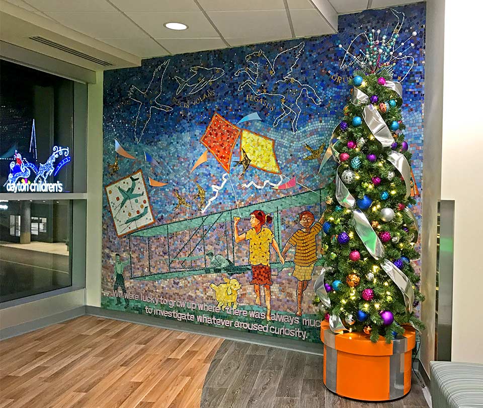 Christmas tree in an orange planter next to a mosaic mural at Dayton Children's Hospital